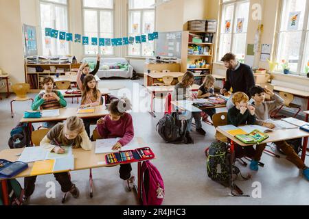 Male and female students studying together while sitting at desk in classroom Stock Photo