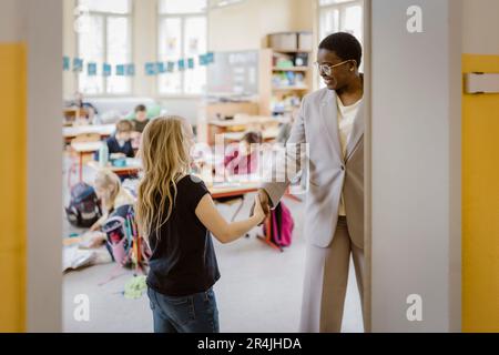 Smiling female teacher doing handshake with schoolgirl in classroom Stock Photo