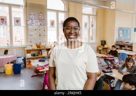 Portrait of smiling teacher standing in front of students at classroom Stock Photo