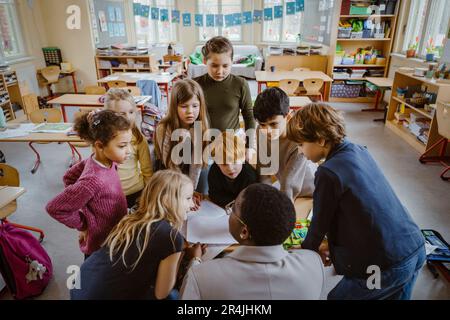 Students looking at teacher helping them in classroom Stock Photo