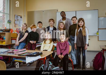 Portrait of smiling teacher and boys and girls against whiteboard in classroom Stock Photo