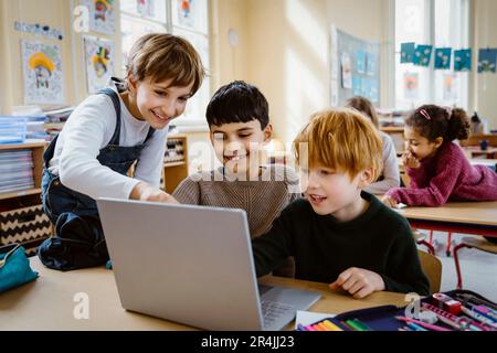 Happy schoolboys using laptop together at desk in classroom Stock Photo