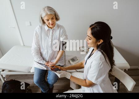 Doctor discussing with senior patient over tablet PC at clinic Stock Photo