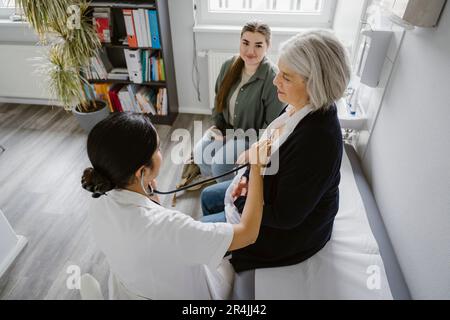 High angle view of female doctor listening heartbeat of senior patient in clinic Stock Photo