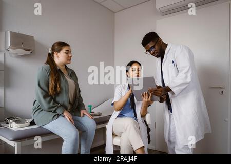 Male and female healthcare workers discussing over tablet PC with female patient in clinic Stock Photo