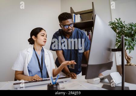 Doctor explaining young male colleague over desktop PC in clinic Stock Photo