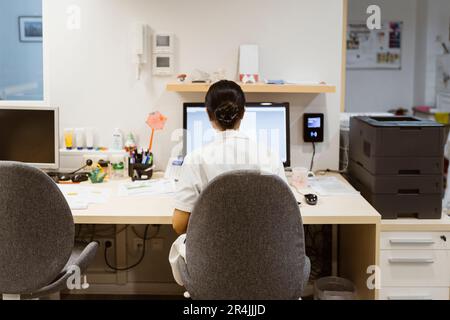 Rear view of female doctor working on desktop computer while sitting on chair at clinic Stock Photo