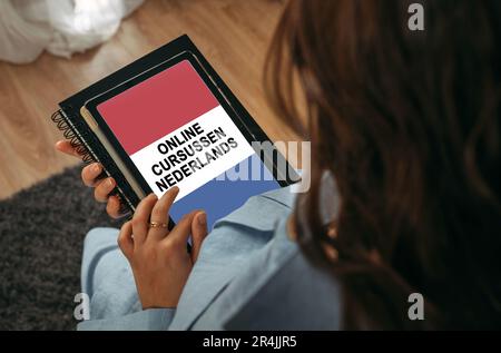 Online learning concept. A woman holds a tablet in her hands on the screen of which it is written - Online Dutch courses. The inscription is in Dutch. Stock Photo