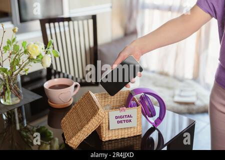 Woman putting phone into box with different gadgets at home Stock Photo