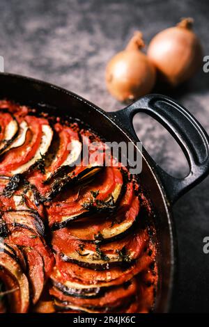 French ratatouille with tomatoes, eggplant, zucchini and fresh herbs in a cast iron skillet against a dark background. Stock Photo