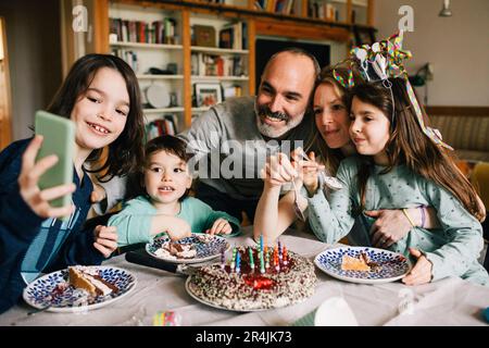 Boy taking selfie with family eating birthday cake while enjoying at home Stock Photo