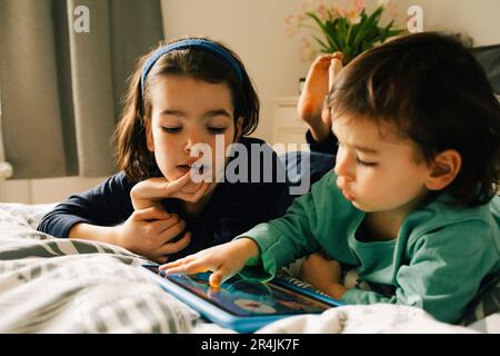 Brothers using digital tablet while lying together on bed at home Stock Photo