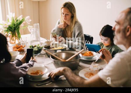 Family using gadgets while sitting at dining table Stock Photo