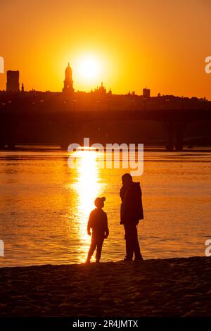 Kyiv. Ukraine, May 2023, a man with his sun enjoying the sunset on a beach in Kyiv with a beautiful view of the Pechenrsk Lavra monastery Stock Photo