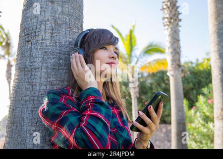 A young woman listens to music with her headphones and her smartphone Stock Photo