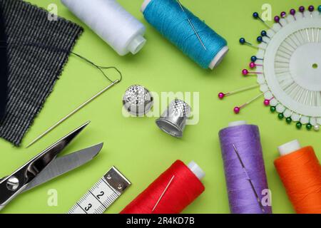 Flat lay composition with thimbles and different sewing tools on green background Stock Photo