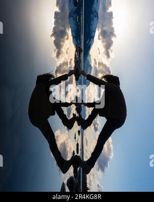 Unique view of a person with reflection in a natural lake with clouds and mountains in background. Awesome perspective of person. Stock Photo