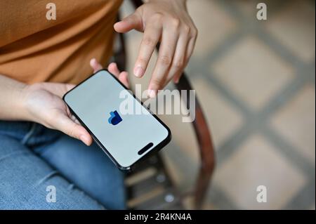 Chiang Mai, Thailand - May 26 2023: Close-up image of a female using PayPal application on her iPhone while relaxing outdoors. Online mobile banking c Stock Photo