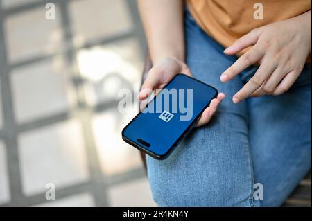 Chiang Mai, Thailand - May 26 2023: Close-up image of a woman login on her LinkedIn profile on her smartphone while sitting outdoors. Stock Photo