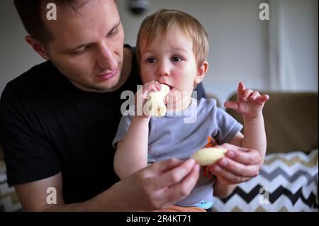 Little toddler eating banana held by his father Stock Photo