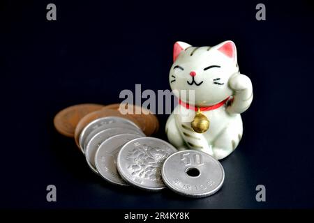 Closed-up of tiny handmade pottery of Maneki-neko, the lucky cat and Japanese money on dark background. Stock Photo