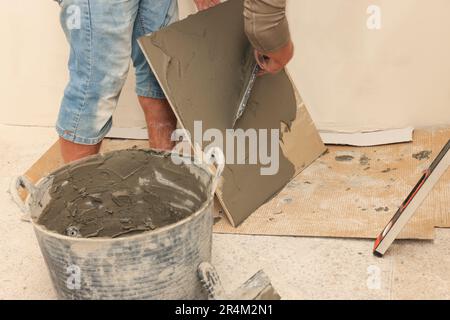 Worker spreading adhesive mix over tile with spatula, closeup Stock Photo