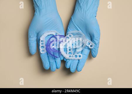 Bite correction. Dentist in medical gloves holding different mouth guards on beige background, top view Stock Photo
