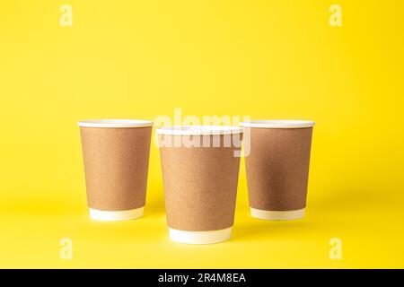 Three paper disposable cups on a yellow background isolated. Stock Photo