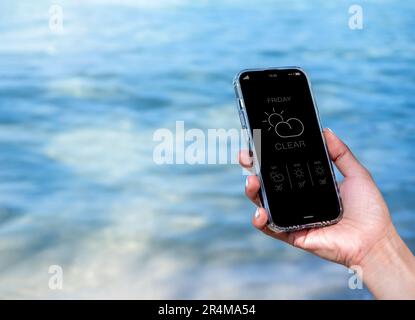 Weather forecast on smartphone. Clear weather, display app on Friday with temperature number, cloud and sun icons on mobile smart phone screen in hand Stock Photo