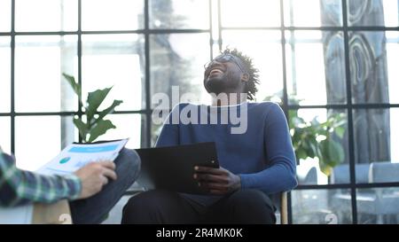 black man with a folder in his hands laughs while sitting Stock Photo