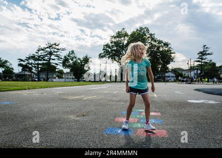 Girl playing hopscotch on blacktop in suburbs Stock Photo