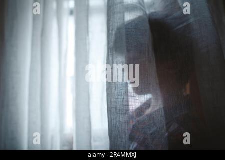 side view silhouette of small child standing behind a window curtain Stock Photo