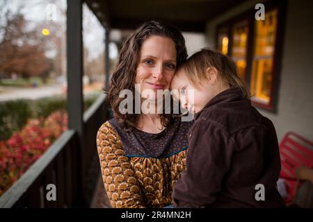 A smiling mom stands outside with a small child nestled in her arms Stock Photo