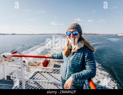 A young woman in a hat smiles while riding a ferry in Portland Maine Stock Photo