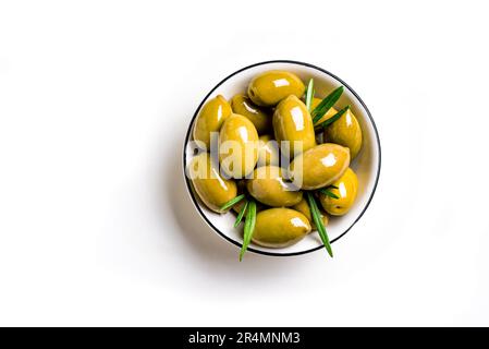 Green olives with rosemary leaves in white bowl, isolated on white background, top view. Stock Photo