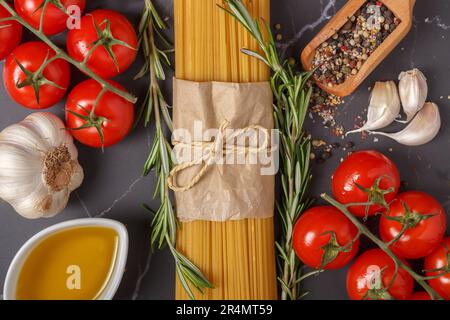 Ingredients for italian pasta. Spaghetti, tomatoes, olive oil, garlic and rosemary on dark gray marble kitchen table . Top view Stock Photo