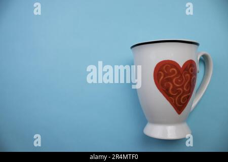 White mug with heart, photographed from above, placed on the edge of a blue background. Stock Photo