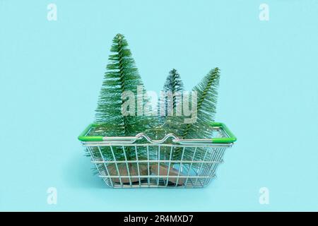 Small Christmas tree is in a shopping cart. Artificial mini Christmas trees in a supermarket trolley on blue background. Christmas, New Year, Holiday Stock Photo