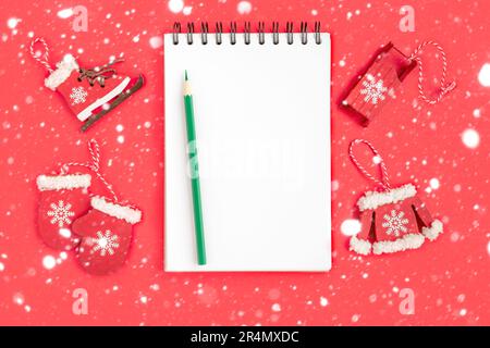 Christmas presents preparation. Notebook, pencil, decorative snowflakes, mitten, sledge, skates on red background. Xmas and Happy New Year composition Stock Photo