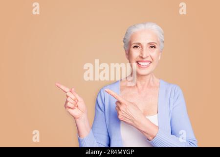Beautiful nice cheerful smiling gray-haired old lady wearing casual, showing pointing way with two fingers. Copy space. Isolated over pastel violet Stock Photo