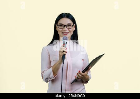 Business woman is giving a speech in microphone. Isolated on pastel yellow. Stock Photo