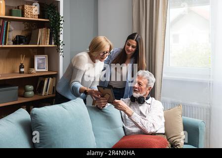 Happy three-generation family hugging sit indoors enjoy time together at home, laughing grown up daughter with 70s dad and middle-aged 50s mom warm re Stock Photo