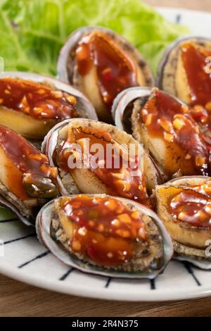 Delicious steamed abalone with spicy tomato sauce, Taiwanese five flavor sauce on wooden table background. Stock Photo