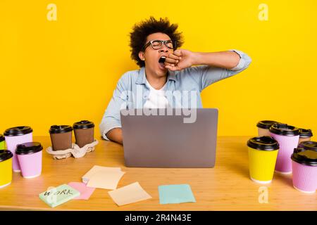 Photo of tired sleepy guy yawning working late night workstation desk netbook coffee cup isolated on yellow color background Stock Photo
