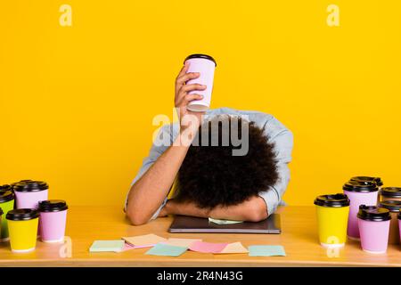 Portrait of exhausted guy hand hold coffee cup fell asleep netbook workplace desk isolated on yellow color background Stock Photo
