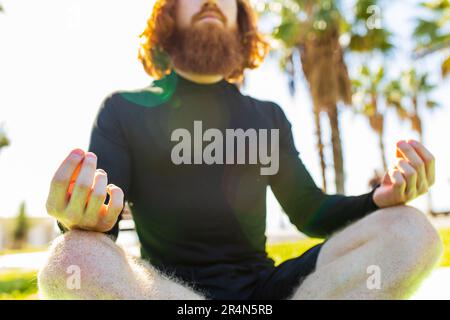 handsome redhaireb man with long beard wear black sporty suit doing yoga meditation in sunny beach Stock Photo