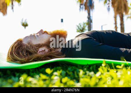handsome redhaireb man with long beard wear black sporty suit doing yoga meditation in sunny beach Stock Photo