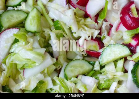 Mixing vegetable salad. Vegetarian salad of radish, cucumbers, cabbage, salt, olive oil. Healthy food. Salad of ripe chopped vegetables is mixed Stock Photo