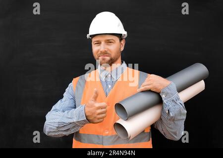 Male Engineer in a White Hard Hats, Orange West. Handsome Confident Build Worker with Blueprints Isolated on Blank Black Background. Copy Space. Indus Stock Photo
