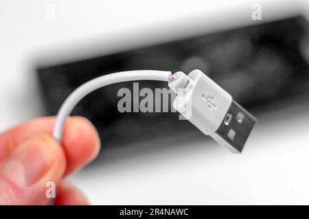 Torn smartphone charging cable in hand closeup with an electronic gadget on the background Stock Photo